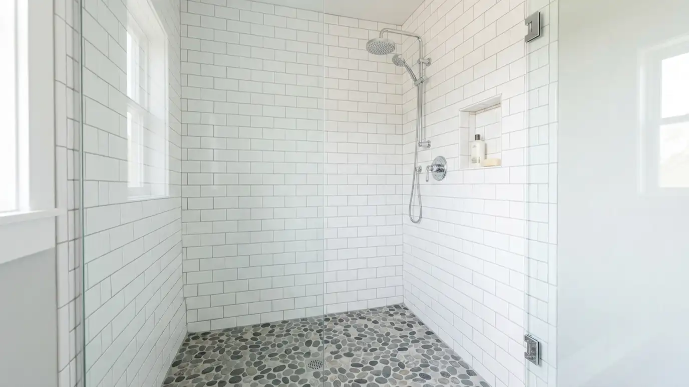 A tiled shower stall with white subway tile walls, a gray pebble floor and a chrome shower head